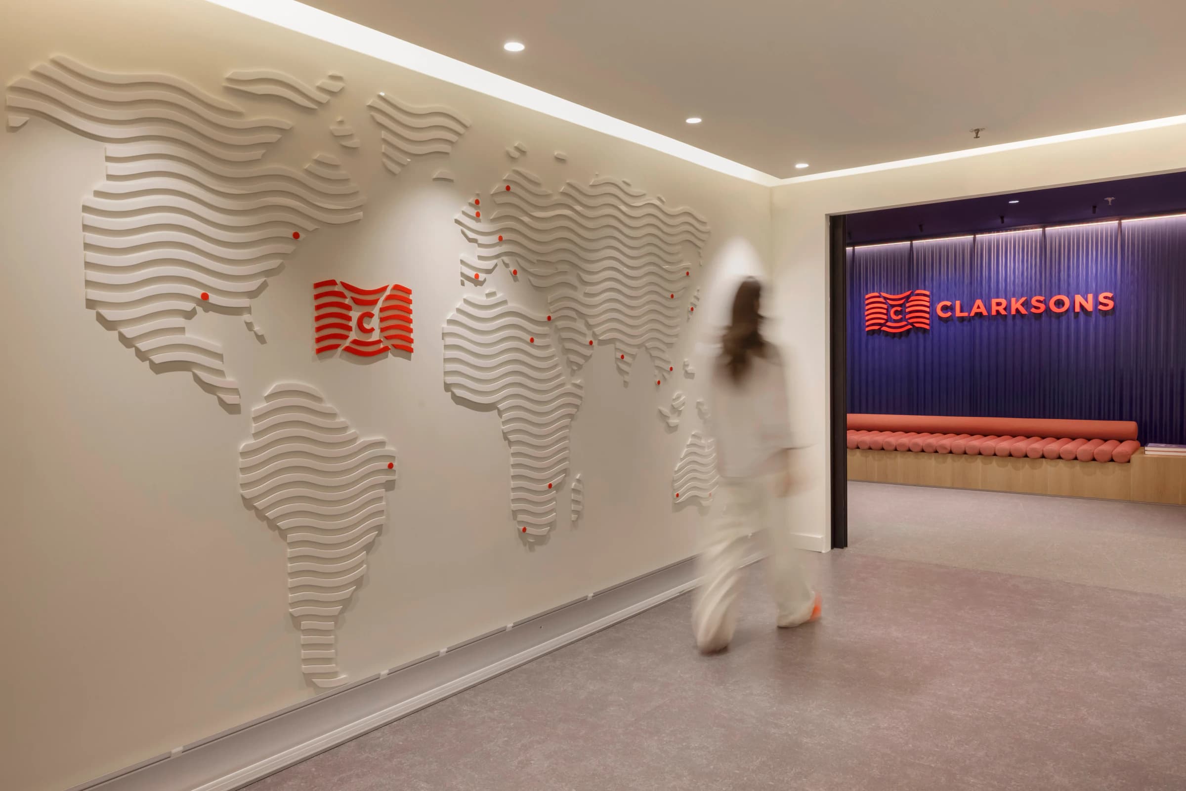 Clarksons reception in Athens: a world map of white relief waves on the wall, the red Clarksons logo and a person walking past