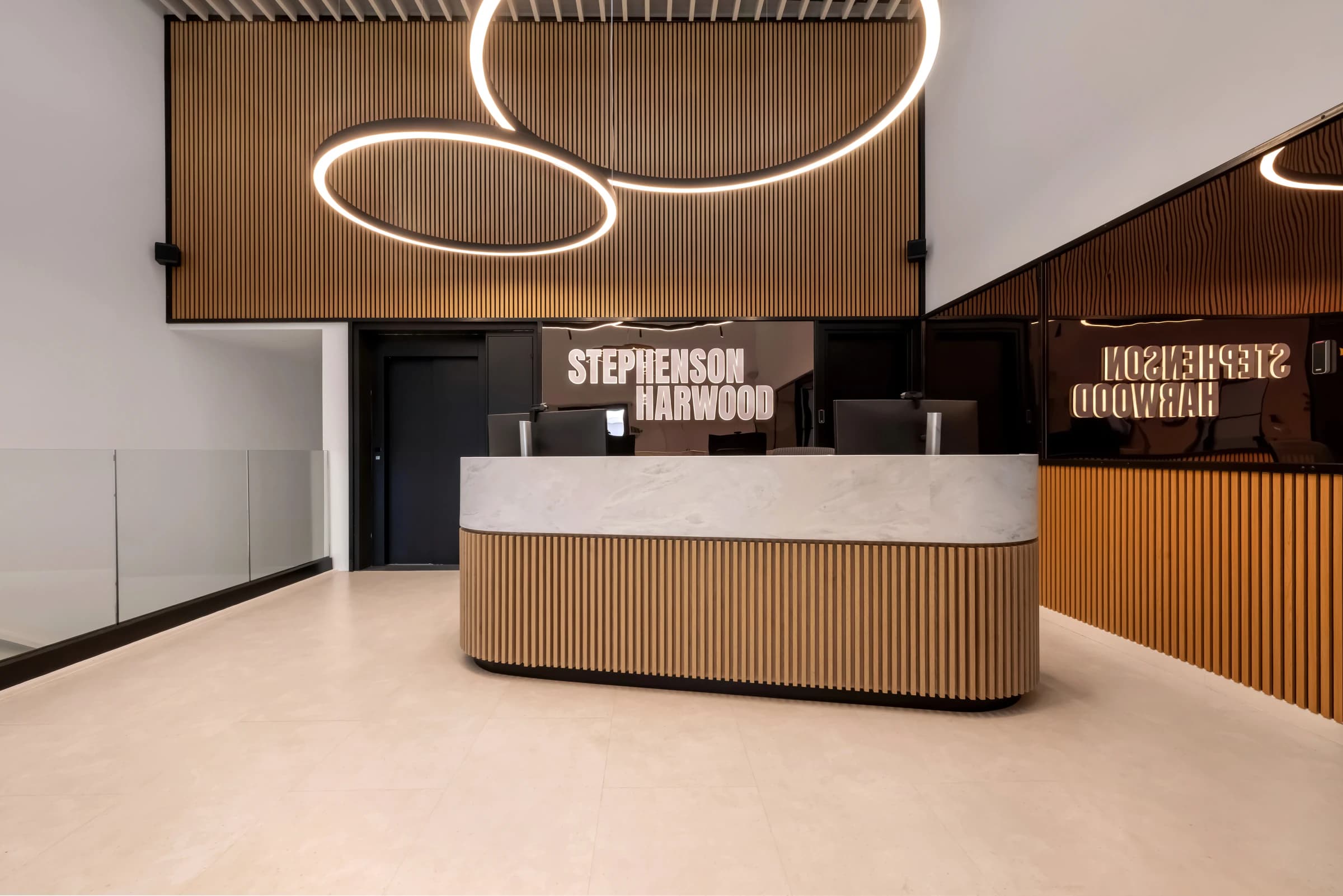 Stephenson Harwood reception: a wooden desk under circular ceiling lights, with the firm’s name on the dark wall behind